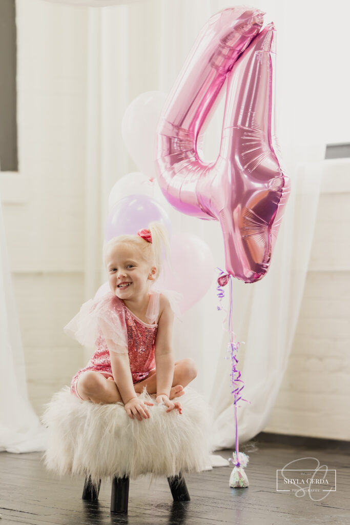 Fourth birthday milestone photos with pink and purple balloons.